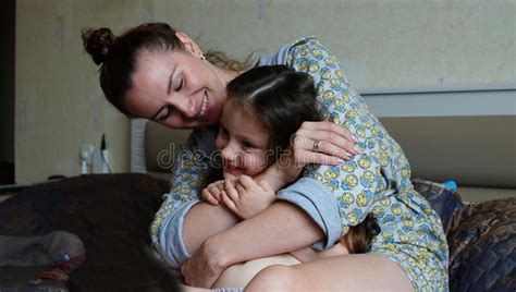 Happy Smiling Girl With Mother Hugging On Sofa At Home Stock Photo