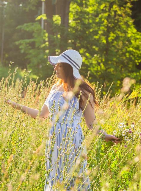 una joven feliz con el pelo largo en el sombrero y el vestido empuja sus manos hacia las plantas