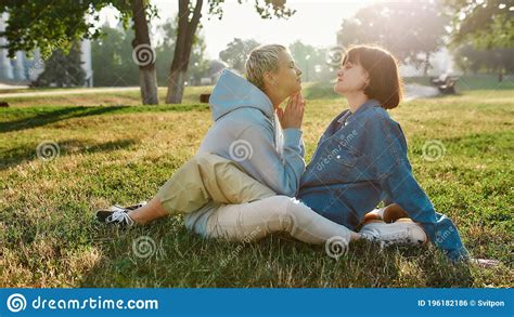 happy lesbian couple of girls looking at each other while sitting on the grass in summer park