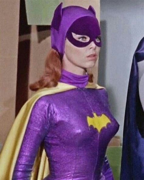 A Woman Dressed As Batman Standing Next To A Man In A Purple Suit And