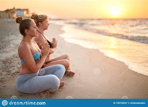 Two Authentic Women Doing Group Yoga Meditation On The Beach At Sunrise