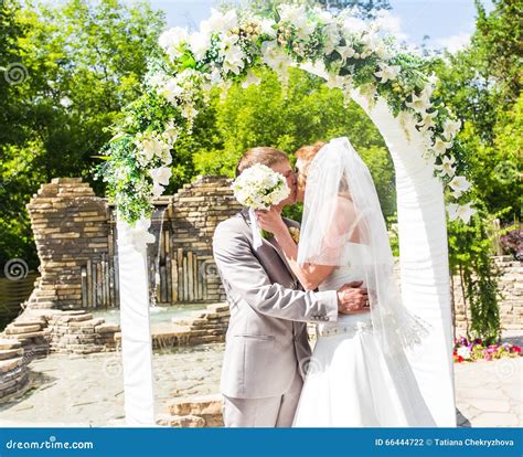 First Kiss Of Newly Married Couple Under Wedding Arch Stock Photo