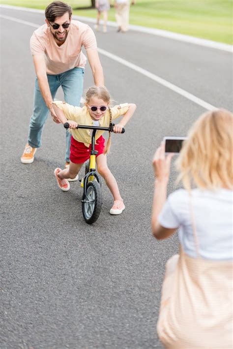 woman with smartphone photographing happy father and daughter riding bicycle stock image image