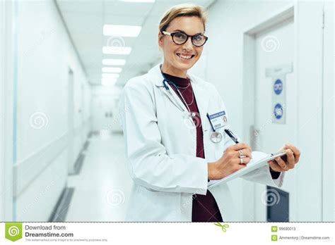 Smiling Doctor Standing In Hospital Corridor With Clipboard Stock Image