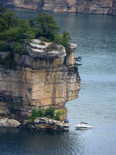 There Is A Boat That Is In The Water Near Some Rocks And Trees On An Island