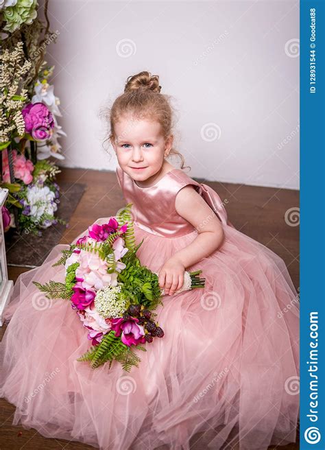 A Little Princess In A Beautiful Pink Dress Sits On The Floor Near