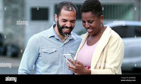 Interracial Couple Laughing In Street Holding Cellphone Candid Mixed Couple Relationship
