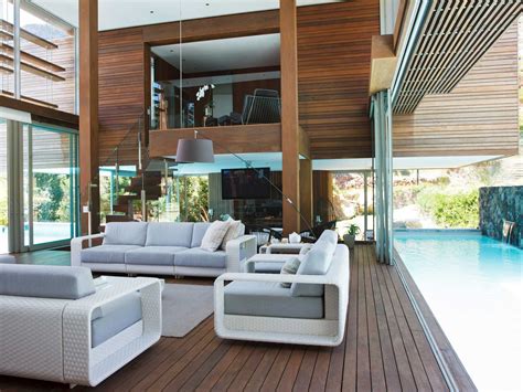 a living room filled with white furniture next to a swimming pool on top of a wooden floor