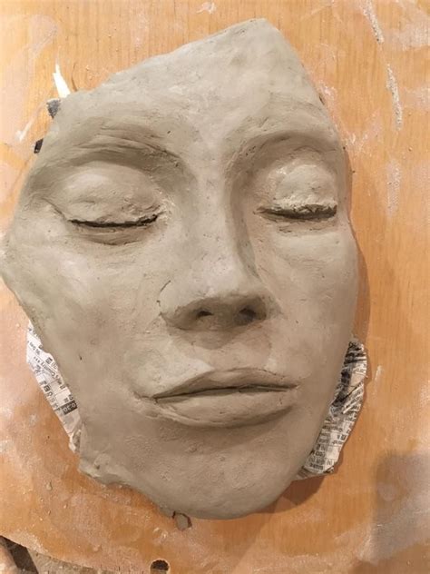 A Clay Face Sitting On Top Of A Piece Of Wood