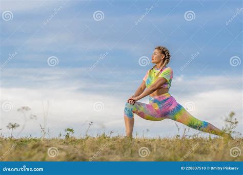 Girl Athlete In Bright Suit Does Exercise To Stretch Muscles Of Legs Against Background Of Blue