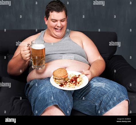 Algo para lavar su comida Un joven obeso sentado en un sofá y se jordeaba con cerveza y comida