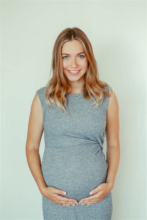 Caucasian Blonde Pregnant Woman In Grey Dress Touching Her Belly Stock