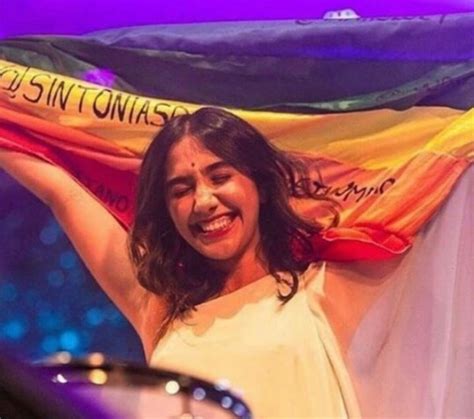 A Woman Holding A Flag In Front Of Her Face And Smiling At The Camera While Standing On Stage