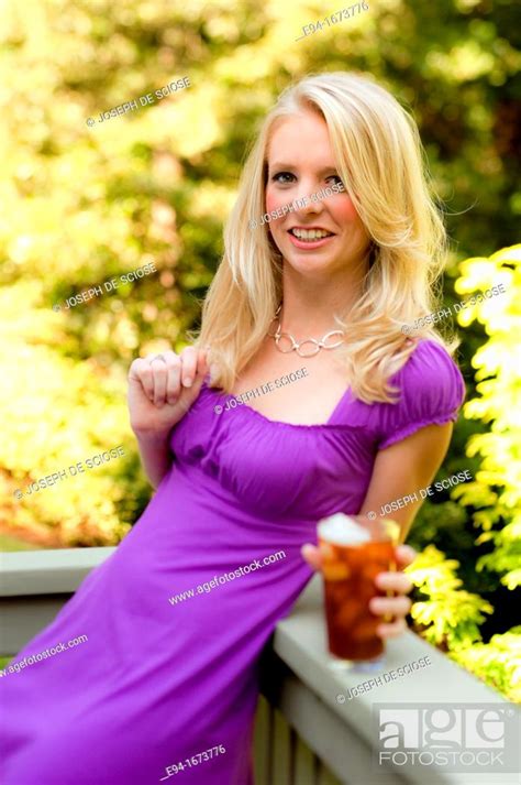 portrait of a 20 year old blond woman in a fuschia dress outdoors with a glass of iced tea