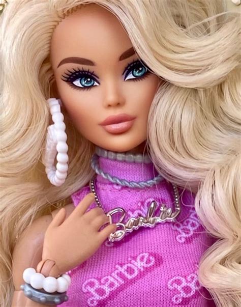 A Barbie Doll With Blonde Hair And Blue Eyes Wearing A Pink Sweater Holding A White Beaded Necklace