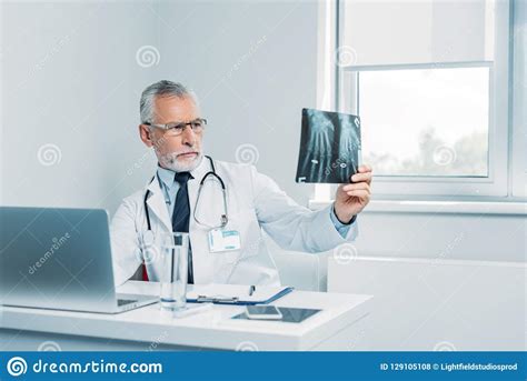 Concentrated Mature Male Doctor Analyzing X Ray Picture At Table Stock