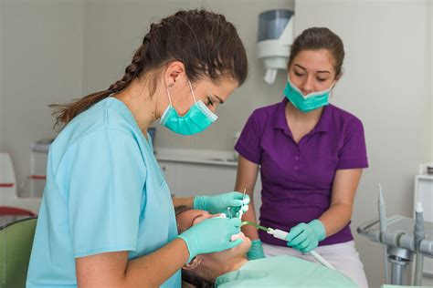 Female Dentist Assisted By Nurse Treating Patient In Dental Office By