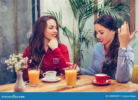 Two Beautiful Young Women Sitting In A Cafe Drinking Coffee And Having