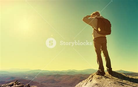 Man Standing At The Edge Of A Cliff Overlooking The Mountains Below