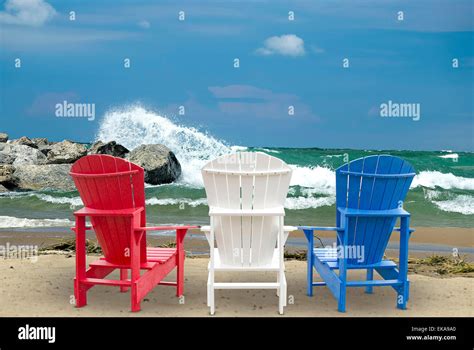Red White And Blue Adirondack Beach Chairs In Sand On The Seashore