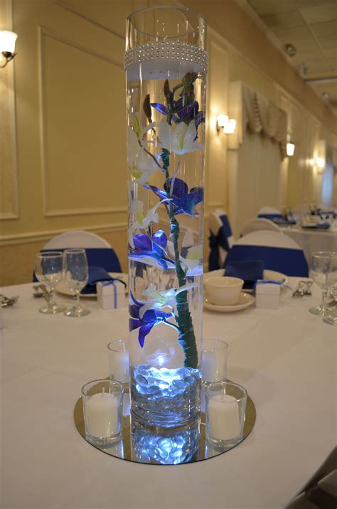 A Tall Glass Vase Filled With Blue Flowers On Top Of A White Table