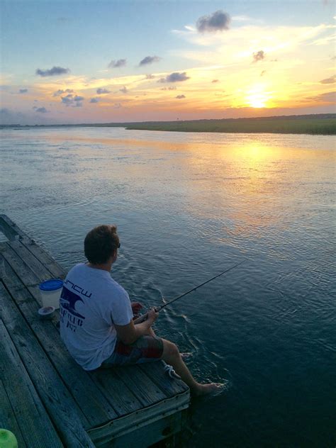 A Man Sitting On A Dock Fishing At Sunset