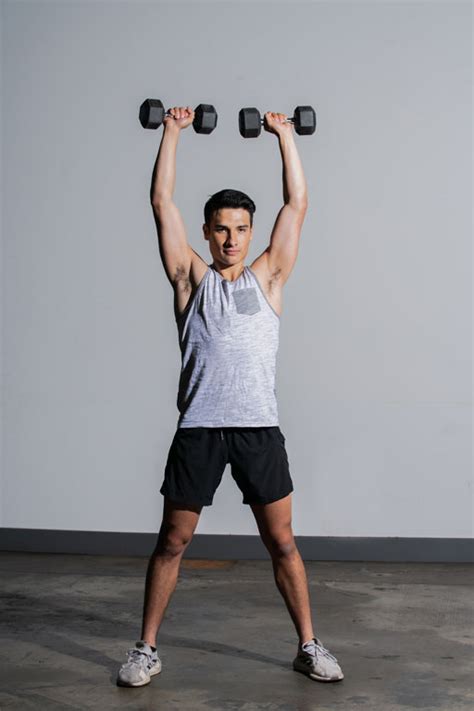 Young Man Lifting Dumbbells Over His Head Showing His Muscle Mass