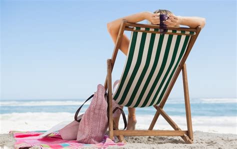 Mulher Sentada Na Cadeira Do Convés Na Praia Com Seu Saco De Praia E Toalha Foto Premium