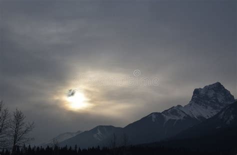 Sunlight Being Blocked By Clouds Over Snowy Mountain Peaks Stock Photo