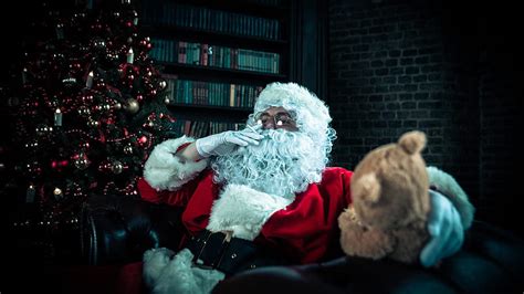 Santa Claus Is Sitting On Couch With Christmas Tree And Books