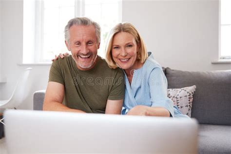 Senior Couple Sitting On Sofa At Home Making Video Call Using Laptop