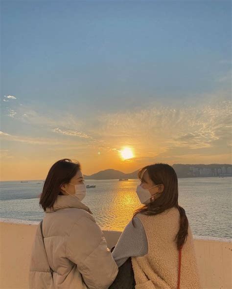 Two Women Sitting On A Wall Looking At The Sunset