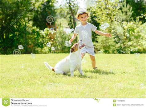 Happy Kid And Pet Dog Playing With Soap Bubbles At