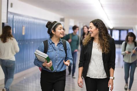 Ethnic Teacher Walking With One Of Her Students Down The Hallway