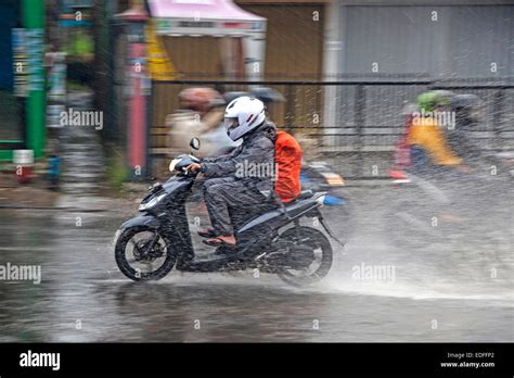 Soaked Indonesian biker riding on scooter during downpour in the rainy
