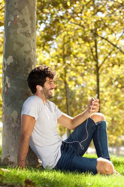 Full Body Laughing Man Sitting Outside With Cellphone And Headphones
