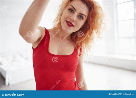 cheerful mood attractive woman in red dress and curly hair in the spacey room near the window