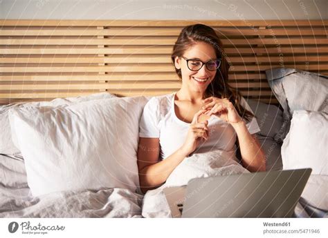 Portrait Of Smiling Young Woman Lying On Bed Using Laptop A Royalty
