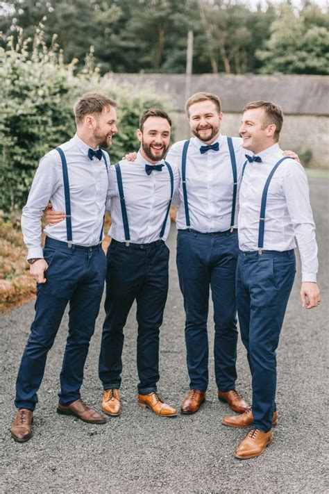 a stylish groom s outfit with navy pants and suspenders light blue shirts navy bow ties brown