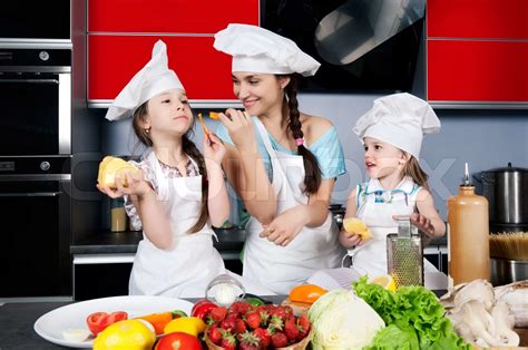 Mom Teaches Two Daughters To Cook At The Kitchen Table With Raw Food Clothing Cooks Stock