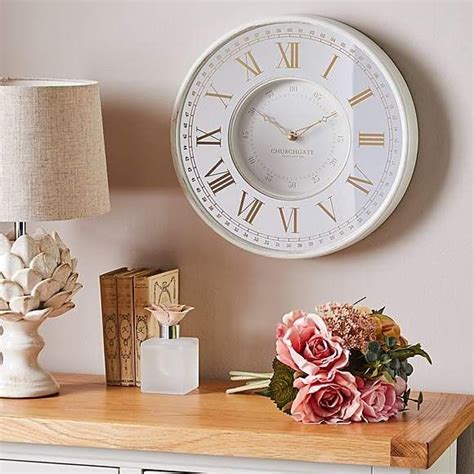 A White Clock Sitting On Top Of A Wooden Table Next To A Vase With Flowers