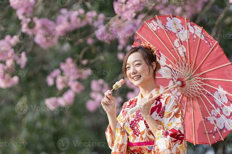 Japanese Woman In Traditional Kimono Dress Holding Umbrella And Sweet Hanami Dango Dessert While