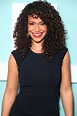 a smiling woman with curly hair and red lipstick wearing a black dress ...