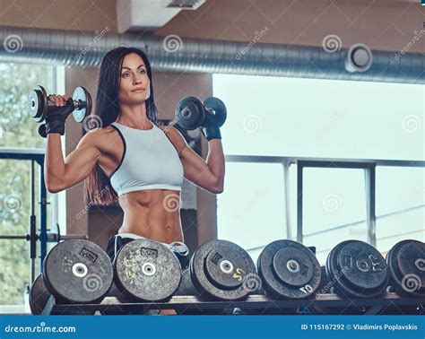 Beautiful Athletic Brunette Female In A Sportswear Doing Exercise On With Dumbbells In The Gym