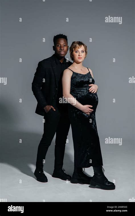 Young African Man And His Caucasian Pregnant Woman Stand Against Grey Background Interracial