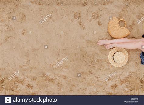 Woman Tanned Legs Straw Hat And Bag On Sand Beach Travel Concept
