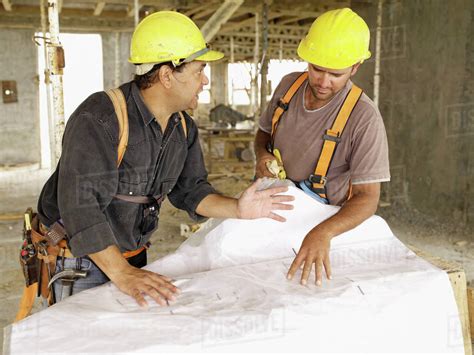 Hispanic Workers Looking At Blueprints On Construction Site Stock