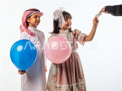 خلفية بيضاء لصبي وفتاه صغيران سعوديان مبتسمان ، الفتاه الصغيرة تأخذ العيدية بيدها والأخرى تمسك