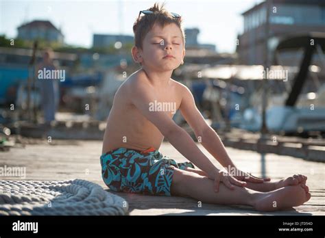 Meditating Cute Little Boy Sitting On Pier Closing His Eyes Stock Photo