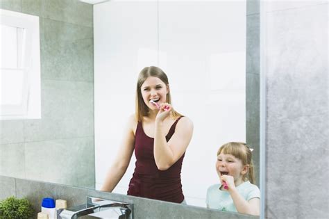 mother and daughter brushing teeth near mirror photo free download